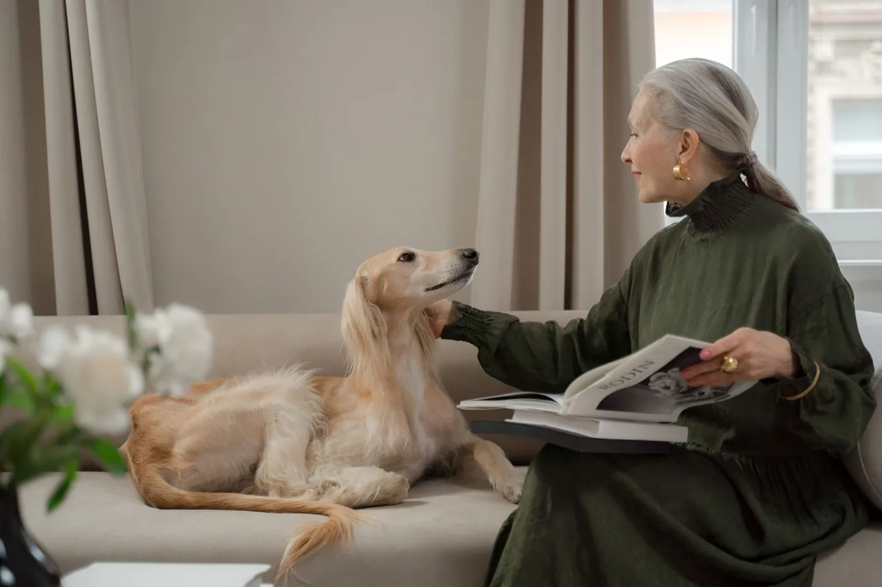 Una mujer lee en un sillón junto a su perro, que descansa.