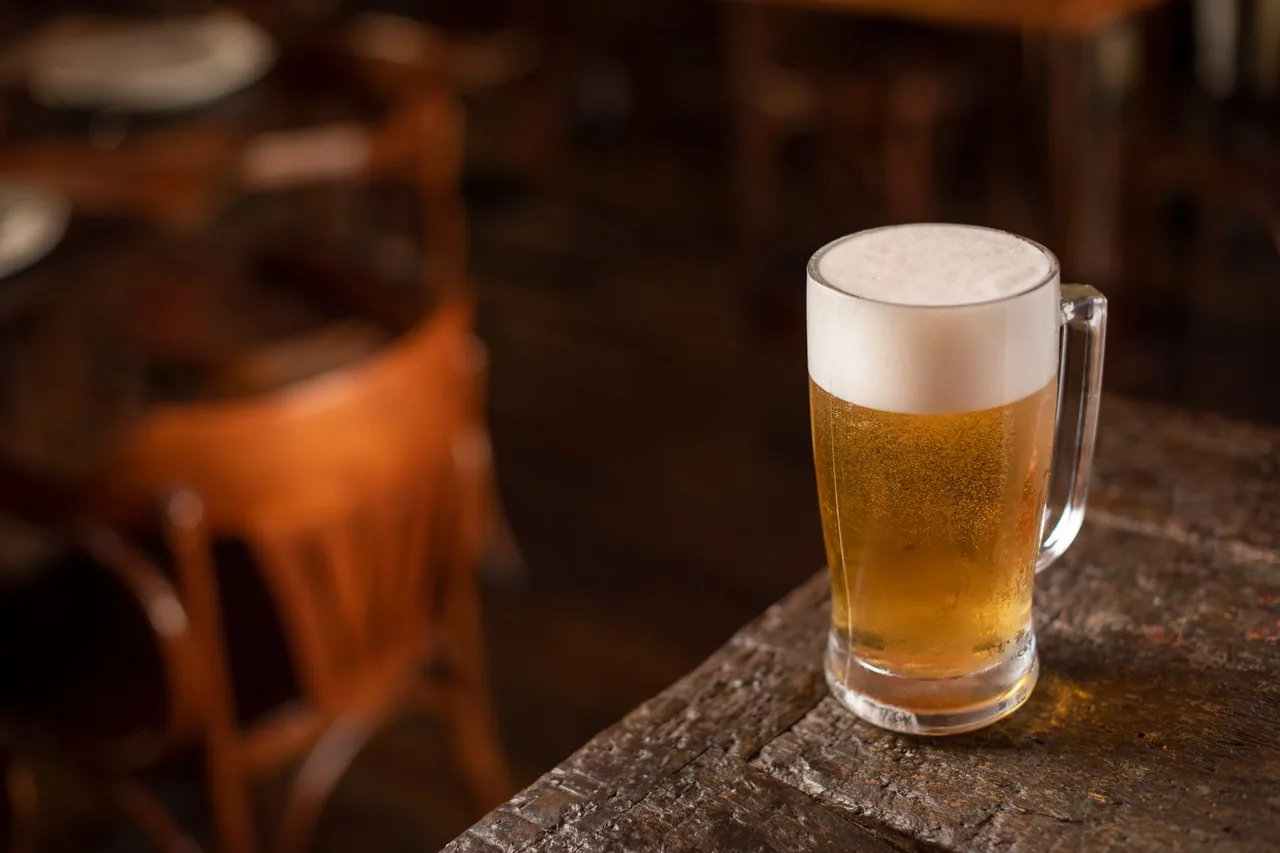 Un tarro de cerveza con espuma sobre una mesa de madera en un bar con poca luz.