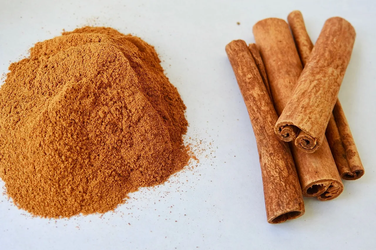Un montoncito de canela molida junto a un manojo de rajas de canela.