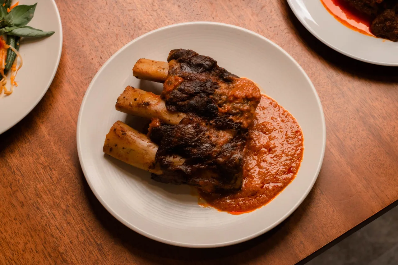 Cooked beef short ribs in sauce on a plate, with the bones sticking out.