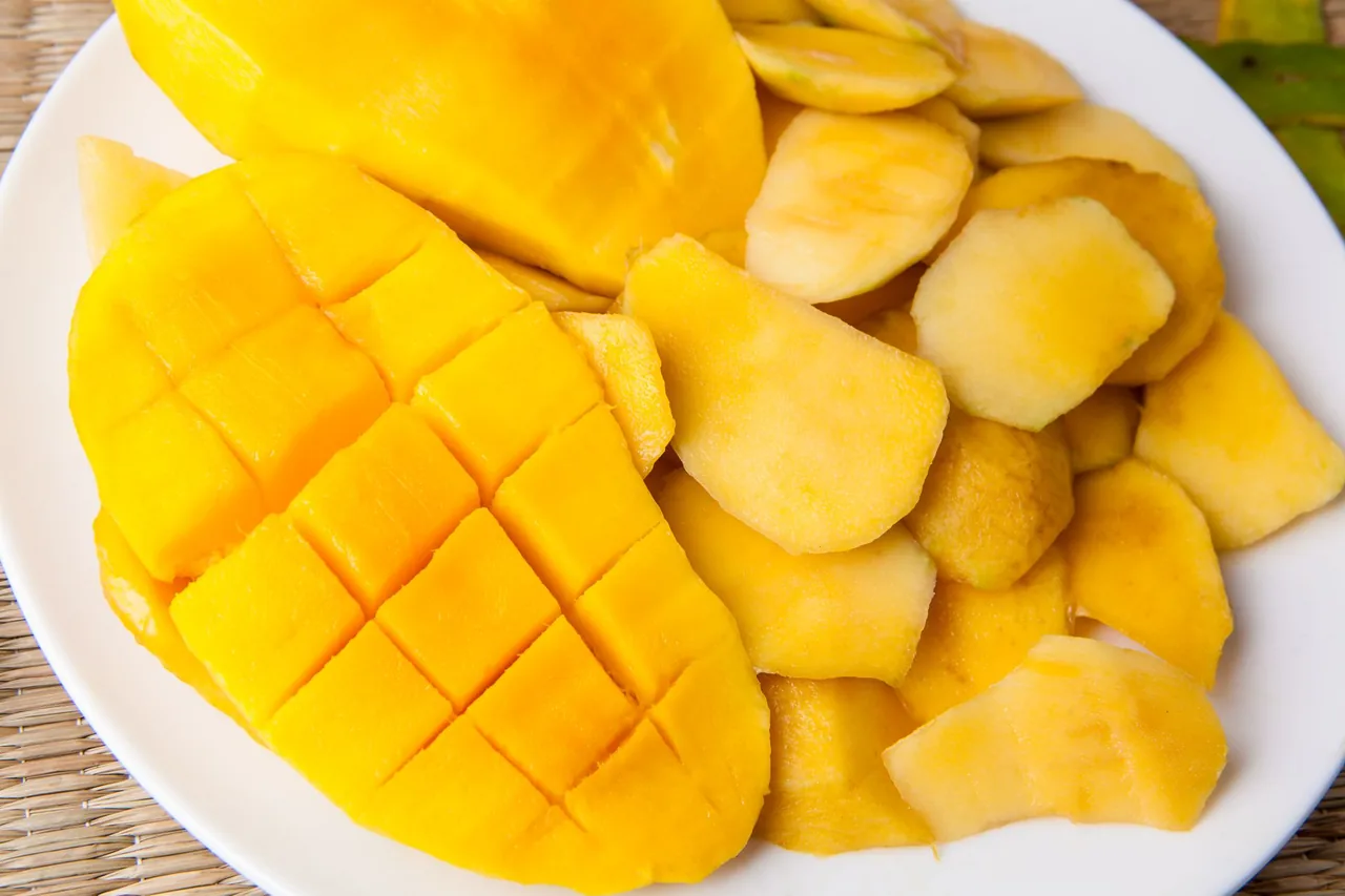 Ripe mango flesh, scored and cubed, on a white plate.