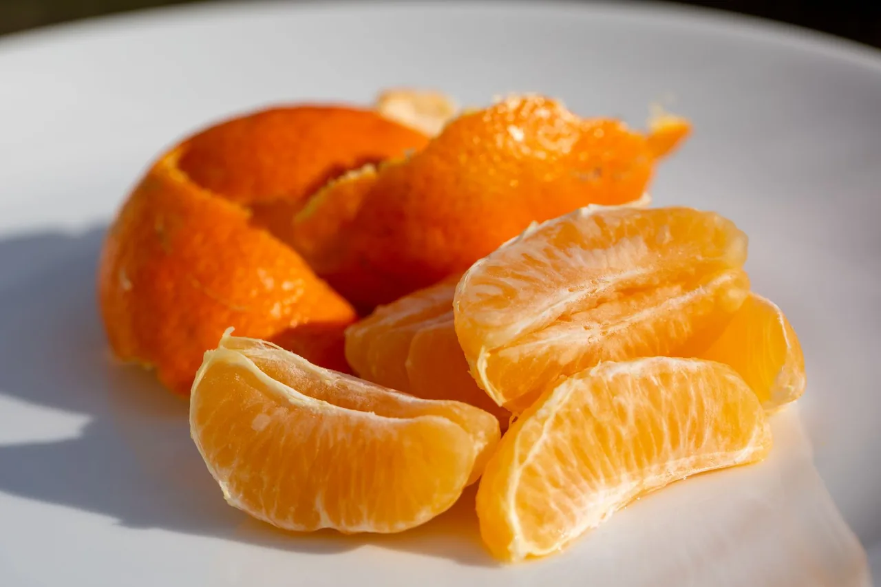 Peeled orange segments next to the peel on a white plate.