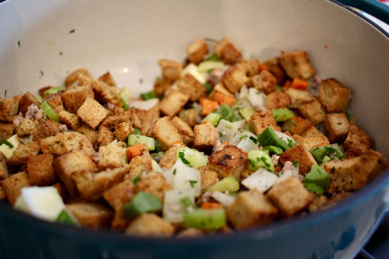 A pot of homemade bread stuffing with toasted bread cubes, diced celery, onion and carrot, crumbled sausage and chopped parsley.