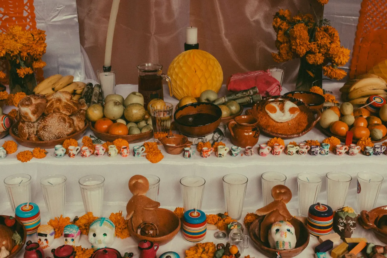 A Day of the Dead ofrenda with bread, fruit, sugar skulls, candles and orange cempasúchil marigolds.