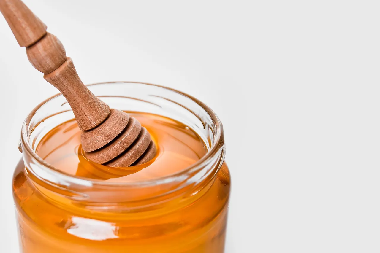 A glass jar of honey with a wooden honey dipper.