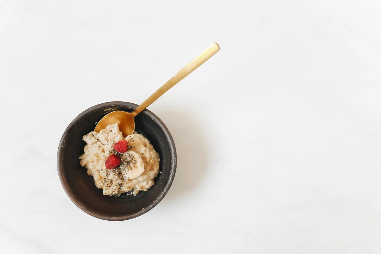 A small dark bowl of oatmeal topped with a little fruit, with a gold spoon.
