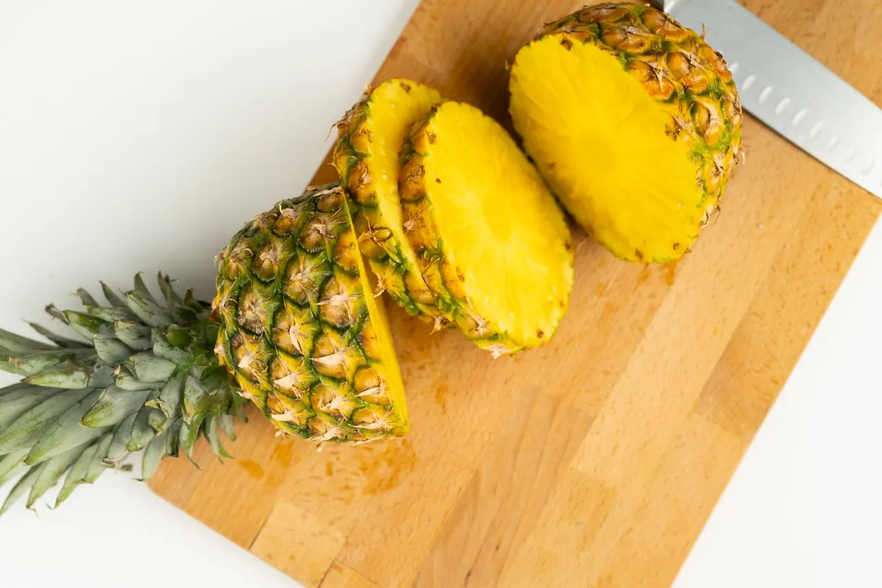 A whole pineapple sliced into rounds on a wooden cutting board.