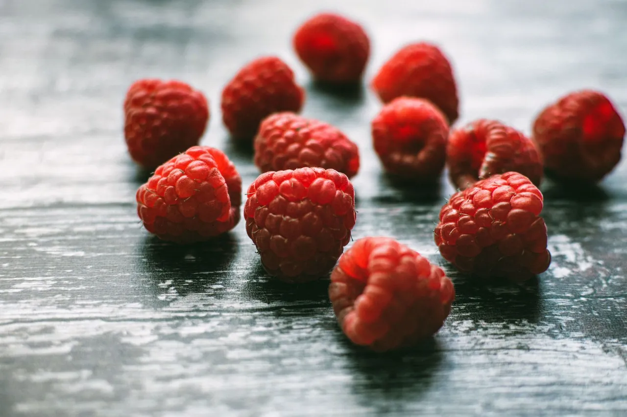 Fresh red raspberries scattered on a weathered wooden table.