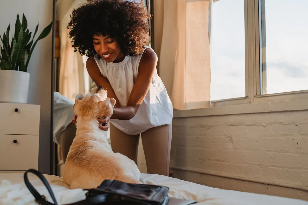 A woman greeting a happy dog indoors.