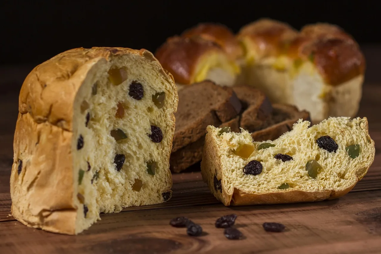 Un panetón partido sobre una mesa de madera, con pasas y fruta confitada a la vista y algunas pasas sueltas al frente.